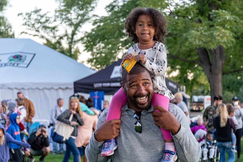 A Black dad smiling with his daughter on his shoulders