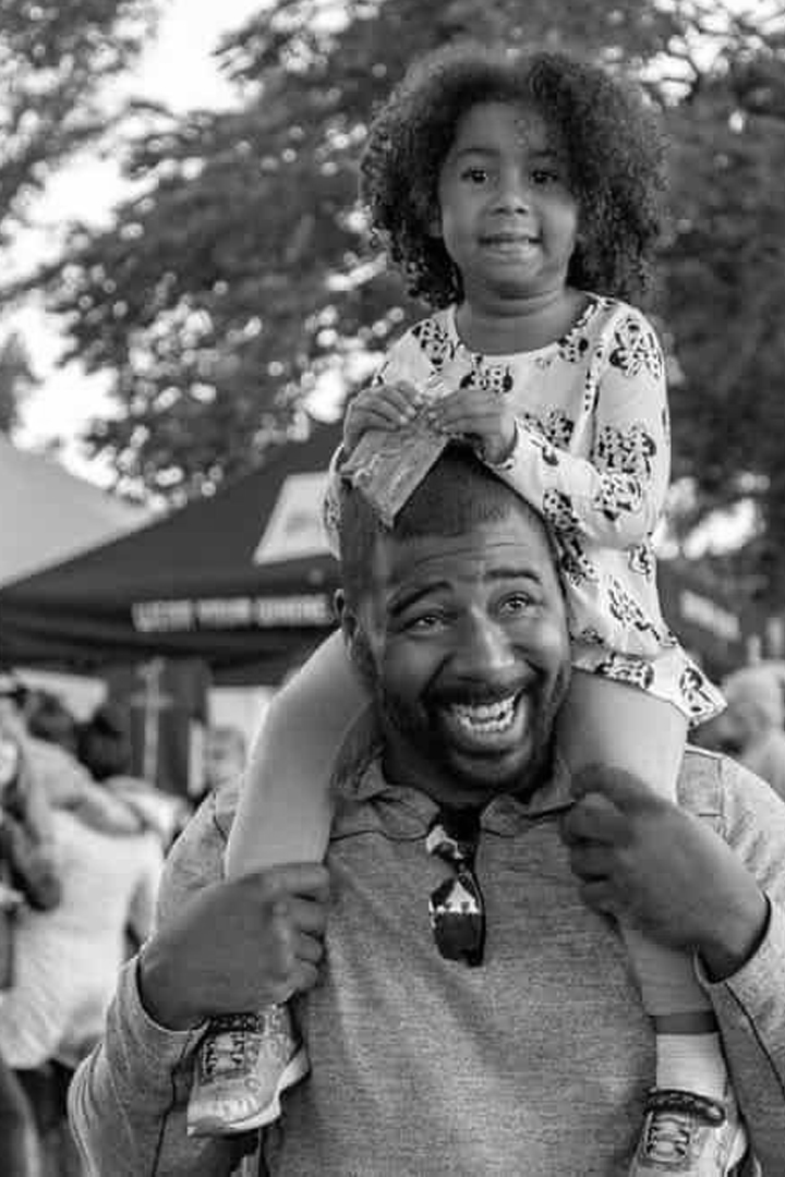 Black and white image of Black dad with his daughter on his shoulders